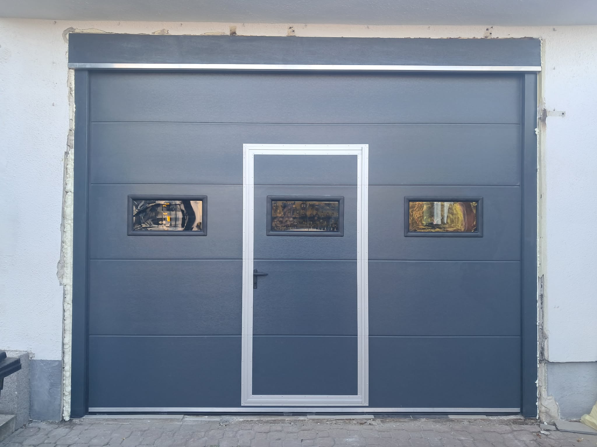 Szara brama z drzwiami serwisowymi i dwoma okienkami