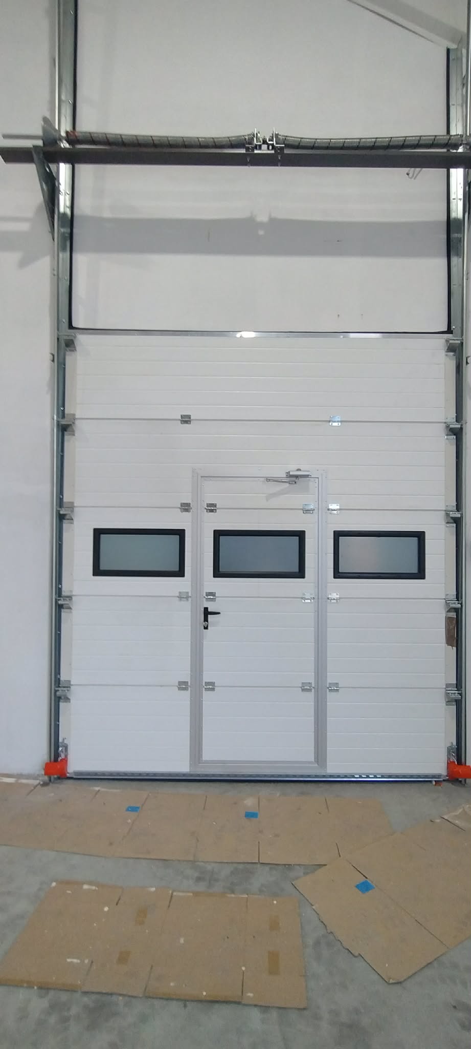 Wysoka biała brama przemysłowa z drzwiami i oknami