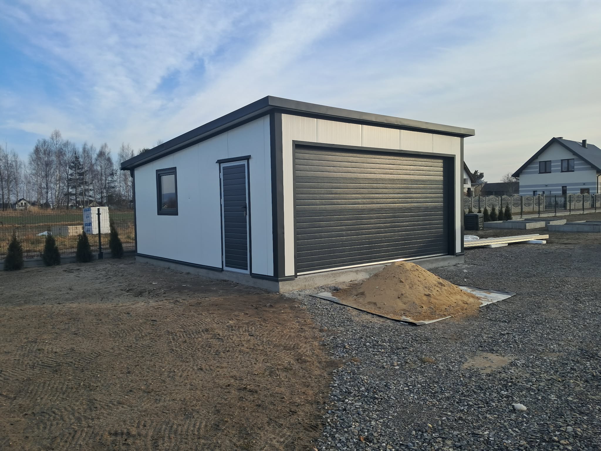 Wolnostojący garaż z szarą bramą i bocznymi drzwiami